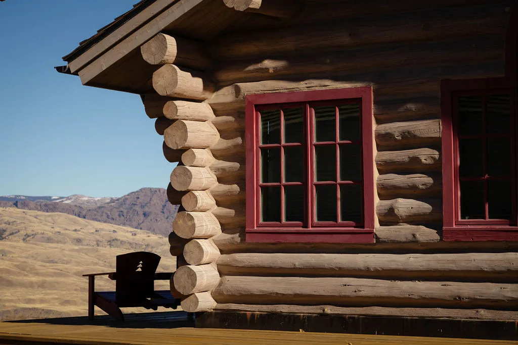 Hand-peeled log cabin detail with red windows and mountain views