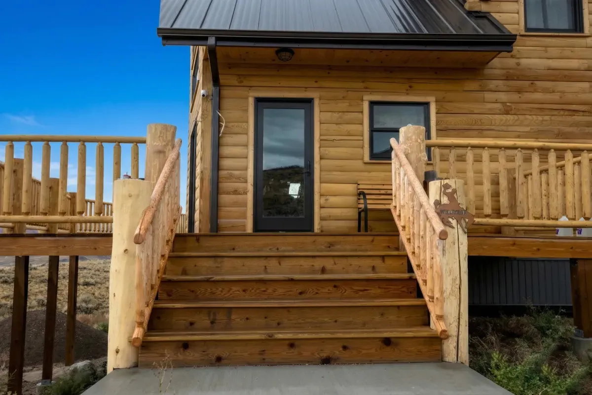 Log cabin entry with custom log railing and stairs by Pilot Peak Construction