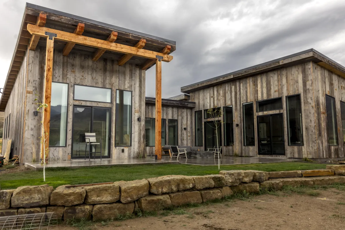 Barnwood home with timber pergola and stone wall by Pilot Peak Construction